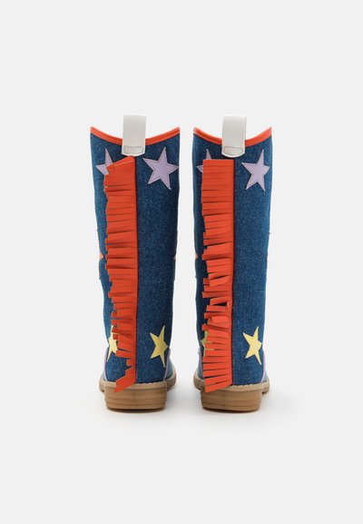 Blå denimstøvler med fargerike stjernedekorasjoner, oransje frynser og en teksturert overflate. Har en hvit løftestropp og en lys brun såle.