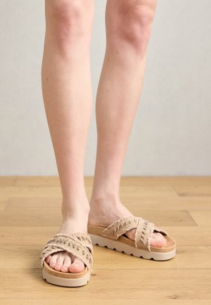 Μπεζ σαγιονάρες με υφασμάτινες λωρίδες σε χιαστή διάταξη και μαξιλαρένιο πάτο, με χοντρή λευκή πλατφόρμα. Φόντο ξύλινο δάπεδο.