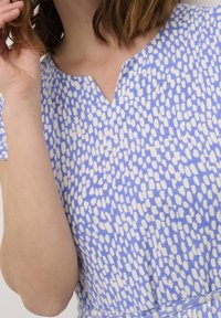 Blaues Baumwollkleid mit V-Ausschnitt und einem weißen abstrakten Muster. Kurze Ärmel und Raffung in der Taille. Glatte Textur.