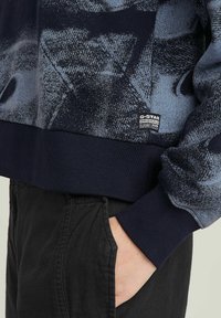 Marineblaue Sweatshirt mit einem strukturierten abstrakten Muster in Blautönen. Gerippte Bündchen und Saum, mit einem G-Star Etikett an der Seite.
