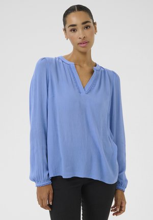 Blouse à manches longues bleu clair avec un décolleté en V, en tissu texturé, avec des poignets élastiques et une coupe décontractée. Présente une délicate finition le long du décolleté.