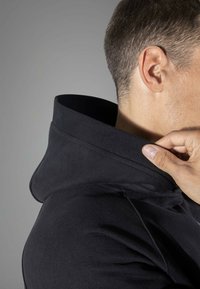Felpa nera con colletto a coste, che mostra un primo piano del collo. Il tessuto sembra liscio, con un design dalla vestibilità rilassata.