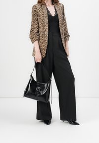 Leopardmönstrad kavaj i texturerat tyg, matchad med en svart spetsblus och höga svarta byxor. Svart läderhandväska med spänne.