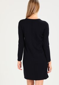 Dunkelblaues langärmliges Kleid mit Rundhalsausschnitt, taillierter Silhouette und dezentem Rückennaht-Detail, gefertigt aus einem weichen Strickstoff.