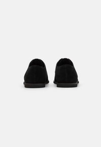 Scarpe nere in suede con profilo basso e punta rotonda. Presentano una sottile suola in gomma e un design minimalista senza decorazioni.