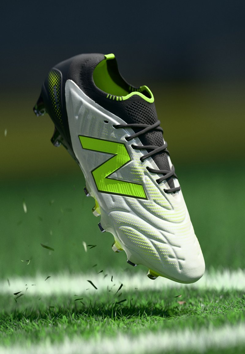 Scarpini da calcio bianchi e verde neon con lacci neri che sollevano l'erba su un campo verde vicino a una linea di confine bianca.