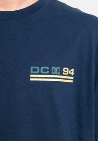 Navy blue T-shirt made of cotton, featuring a graphic in green, yellow, and white reading "DC 94" with two horizontal stripes.