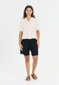 Korte mouwen, lichtgewicht witte blouse met knoopjes, gecombineerd met zwarte losvallende shorts. Draag het met bruine sandalen. Eenvoudig, casual ontwerp.