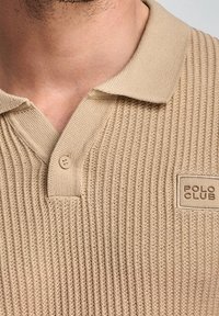 Béžové žebrové polo tričko s plochým límcem, které má zapínání na dva knoflíky a značkovou nášivku "POLO CLUB" na levé straně.