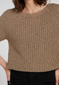 Maglione a maniche corte lavorato a maglia di colore marrone chiaro con texture a coste. Presenta un colletto rotondo e un design leggermente accorciato.