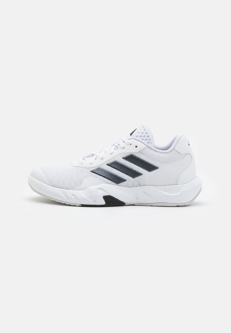 Zapatilla deportiva blanca con parte superior de malla, tres rayas negras en el lateral, puntera texturizada, cuello acolchado y una suela gruesa para soporte.