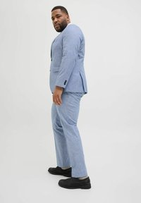 Helles, blaues Anzug aus einem textured Stoff, mit einer slim fit Jacke mit zwei Knöpfen, passenden Hosen und schwarzen Schuhen.