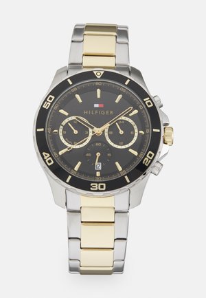 Montre pour homme avec un bracelet en acier inoxydable argenté et doré, cadran noir, accents dorés, fonctionnalités chronographe et affichage de la date. Grands marqueurs numériques.