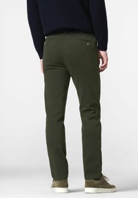Chinos verts à coupe slim, avec des poches arrière dotées de détails en bouton, fabriqués à partir d'un tissu lisse, associés à des baskets de couleur claire.