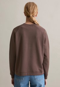 Maglione marrone a collo tondo con maniche raglan, texture morbida e polsini a costine. Abbinato a jeans in denim azzurri.