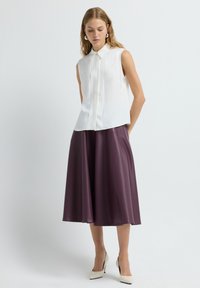 Weiße ärmellose Bluse mit einem Kragen, kombiniert mit einem bordeauxfarbenen plissierten Rock. Glänzende Textur, minimalistische Details und dezente Taillierung.