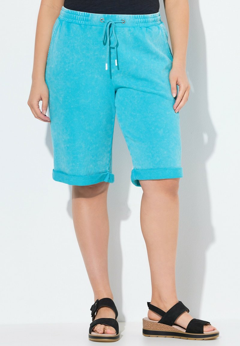 Shorts en mélange de coton turquoise avec des ourlets roulés, taille à cordon de serrage, et deux poches latérales. Assortis à des sandales à talons compensés noires.