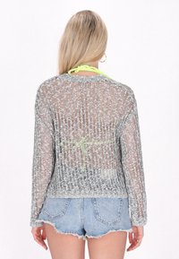 Pilkas megztinis su atviru mezgimu ir ilgomis rankovėmis, turi apvalų iškirpimą ir ryškią žalią juostelę gale.