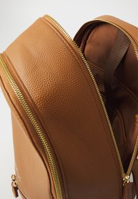 Zaino in pelle marrone con finitura testurizzata, doppie cerniere dorate e un ampio interno con rivestimento in tessuto marrone e tracolla.