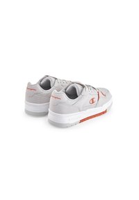Grijze sneakers van mesh en suede materiaal, witte zool, rode accenten, ronde vorm en logo-detail op de hiel.
