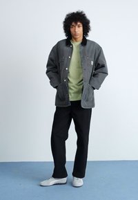 Grau Jacket mit einem schwarzen Kragen über einem hellgrünen Hemd, kombiniert mit schwarzen Hosen und weißen Sneakers. Die Jacke verfügt über Knopfschließungen und Taschen.