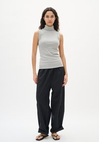 Sivi bezrukavi turtleneck top s rebrastom teksturom, uparen s crnim širokim hlačama. Model stoji u crnim japankama na bijeloj pozadini.