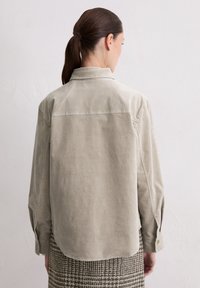 Light beige corduroy shirt with a back yoke, long sleeves, and a rounded hem. Features contrasting stitching and buttoned cuffs.