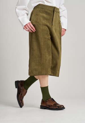 Culottes de ante verde oliva con un ajuste relajado, combinados con zapatos marrones de estampado y calcetines verdes. Cierre simple con botón y cremallera.