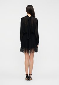 Μαύρο φόρεμα με μακριά, διαφανή μανίκια και κορδόνι στον λαιμό. Διαθέτει δαντελένιο τελείωμα στη βάση. Συνδυάζεται με μαύρες ψηλοτάκουνες γόβες.