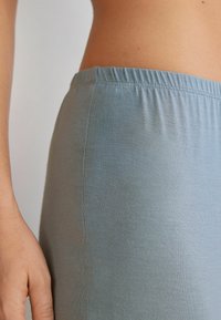 Ljusblå, elastisk tygleggings med elastisk midjeband, slät textur och en figurnära design, visad i sidovy mot en neutral bakgrund.