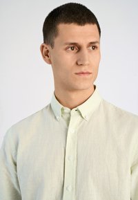 Camicia verde chiaro in lino con colletto classico, texture sottile e bottoni bianchi lungo il davanti.