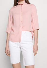 Light pink button-up blouse with a ruffled collar, short sleeves, and textured fabric, paired with white denim shorts.