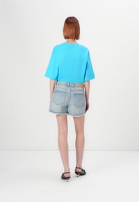 Κοντομάνικη τιάτα σε τυρκουάζ χρώμα, συνδυασμένη με ανοιχτό μπλε τζιν σορτς με ταλαιπωρημένο στρίφωμα και δερμάτινη λεπτομέρεια στη ζώνη.
