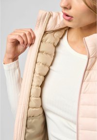 Lichtroze puffer vest met een gladde binnenvoering, voorzien van een rits en een gewatteerde textuur. Gedragen over een crème rib gebreide longsleeve top.