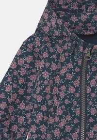 Mörkblå jacka med rosa och vita små blommönster, dragkedja framtill och uppvikt krage.