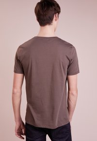 Camiseta de manga corta y cuello redondo en un color marrón apagado, fabricada con suave tela de algodón, con una textura lisa y un corte relajado.