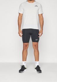 Herrträningsoutfit bestående av en andningsbar vit t-shirt med mönstrad textur, tillsammans med åtsittande svarta shorts och svarta löparskor.