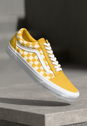 Yellow sneaker with checkered pattern, white accents, and laces. Made from a textured material, featuring a rubber sole and streamlined design.