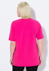 T-shirt fucsia a maniche corte con scollatura rotonda. Tessuto morbido, vestibilità rilassata e orlo posteriore leggermente più lungo. Indossato con pantaloni neri.