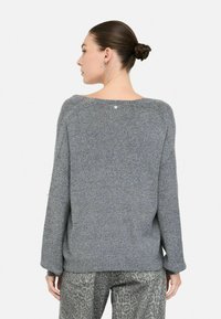 Pull en tricot gris avec une coupe décontractée, col large et poignets côtelés. Présente des détails subtils scintillants et un petit logo au dos.