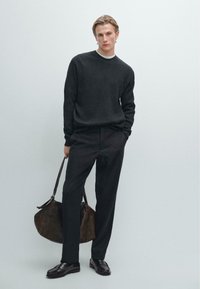 Maglione nero a coste, pantaloni neri e mocassini neri. Porta una borsa in pelle marrone. Look semplice e rilassato con materiale testurizzato.