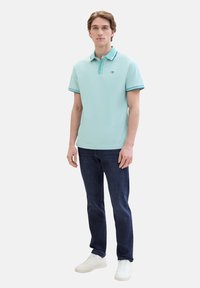 Lichtblauwe polo met gestreepte kraag en boorden, gecombineerd met donkerblauwe jeans en witte sneakers. Casual fit met korte mouwen.