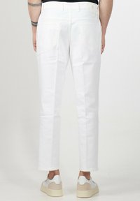 Pantaloni in denim bianco con gambe dritte, tasche posteriori e dettagli di cucitura discreti, abbinati a sneaker bianche.