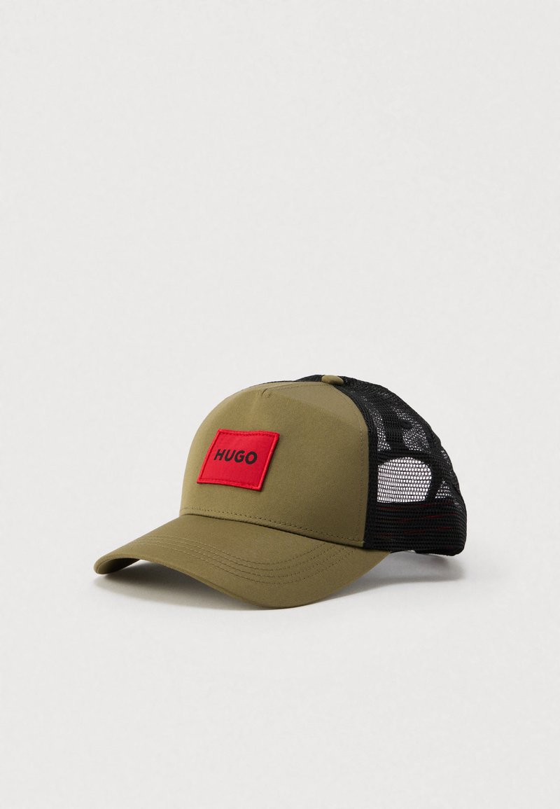 Καπέλο σε ελαιώδες πράσινο με κόκκινο ορθογώνιο μπαλώμα που γράφει "HUGO", με μαύρα δίχτυα στο πλάι, καμπυλωτό γείσο και λείο υλικό.