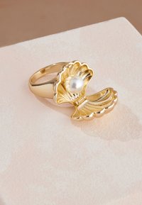 Zlati prstan v obliki odprte školjke s centralno belo biserno kroglico. Detajli školjke so teksturirani z gladkim sijajnim zaključkom.