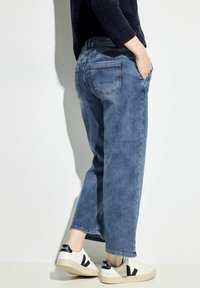 Jeans de mezclilla en azul claro con un corte relajado, que cuentan con bolsillos traseros y un leve desvanecimiento. Combinados con zapatillas blancas con acentos negros.