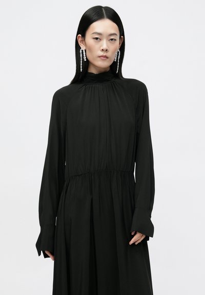 Čierne šaty s dlhým rukávom a vysokým golierom, s r gathered pásom a splývavou sukňou. Hladká textúra s jemným leskom. Obsahuje zvonové rukávy a drapériu.
