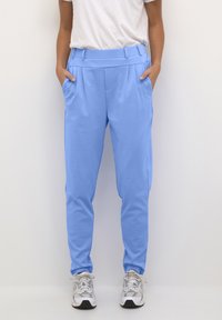Lichtblauwe tapered broek van zachte stof, met zijzakken, een platte voorkant en een zachte textuur. Draag ze met zilveren sneakers.