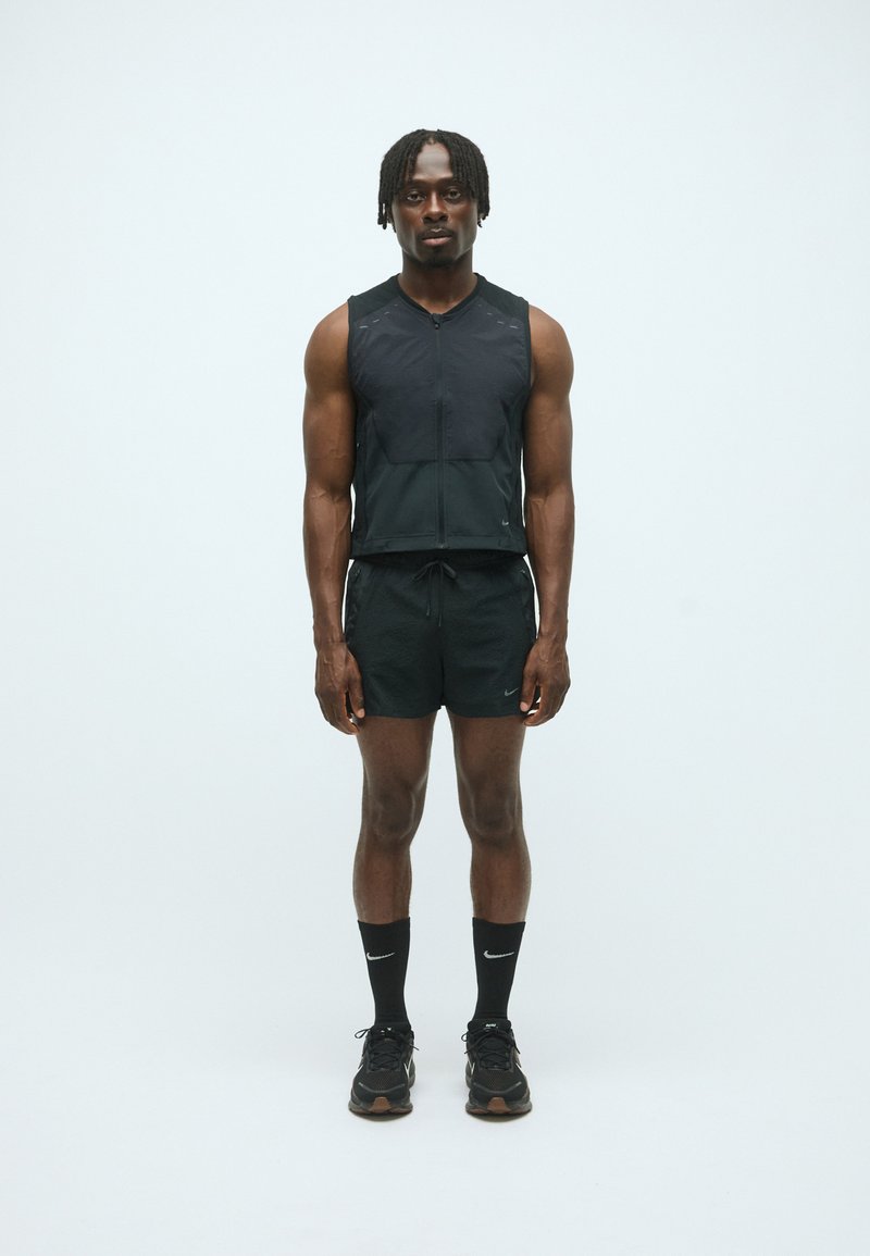 Zwarte sportieve vest met rits, gecombineerd met zwarte shorts. Gekleed met zwarte Nike sokken en sneakers. Slim fit, lichtgewicht stof, minimalistisch ontwerp.