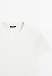 White cotton t-shirt with a round neckline and short sleeves. Ribbed texture, minimalistic design, and a small black label at the neck.